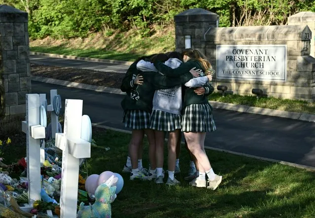 Girls embrace in front of a makeshift memorial for victims by the Covenant School building at the Covenant Presbyterian Church following a shooting, in Nashville, Tennessee, March 29, 2023. A heavily armed former student killed three young children and three staff in what appeared to be a carefully planned attack at a private elementary school in Nashville on March 27, 2023, before being shot dead by police. Chief of Police John Drake named the suspect as Audrey Hale, 28, who the officer later said identified as transgender. (Photo by Brendan Smialowski/AFP Photo)
