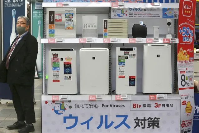 A man wearing a face mask to protest against the coronavirus stands beside a display of air cleaners at an electronics retailer in Tokyo, Tuesday, January 12, 2021. The Tokyo area has been under a state of emergency since Friday to try to stop the spread of the virus. The banner at bottom reads: “Antivirus”. (Photo by Koji Sasahara/AP Photo)