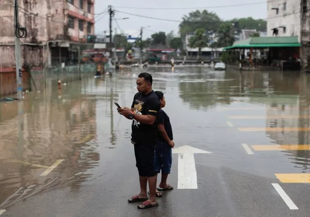 A man and a child stand on a road partially submerged under the floodwaters at Kota Tinggi, Johor, Malaysia on March 5, 2023. (Photo by Hasnoor Hussain/Reuters)
