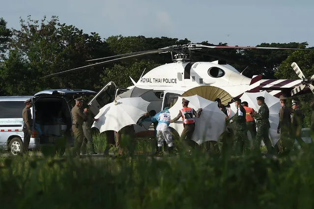 Police and military personnel use umbrellas to cover around a stretcher near a helicopter and an ambulance at a military airport in Chiang Rai on July 9, 2018, as rescue operations continue for those still trapped inside the cave in Khun Nam Nang Non Forest Park in the Mae Sai district. Four boys among the group of 13 trapped in a flooded Thai cave for more than a fortnight were rescued on July 8 after surviving a treacherous escape, raising hopes elite divers would also save the others soon. (Photo by Lillian Suwanrumpha/AFP Photo)