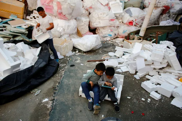 Children use a tablet computer as a man breaks styrofoam at a recycling yard at the edge of Beijing, China, September 21, 2016. (Photo by Thomas Peter/Reuters)