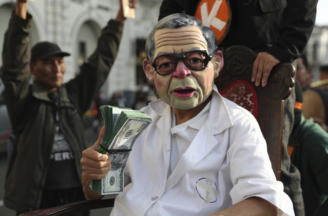 An actor wearing a mask depicting former president Alberto Fujimori performs with fake money during a protest, in Lima, Peru, Wednesday, October 17, 2018. TAn appeals judge has freed Peru's opposition leader Keiko Fujimori a week after she was arrested during a money laundering investigation. (Photo by Martin Mejia/AP Photo)