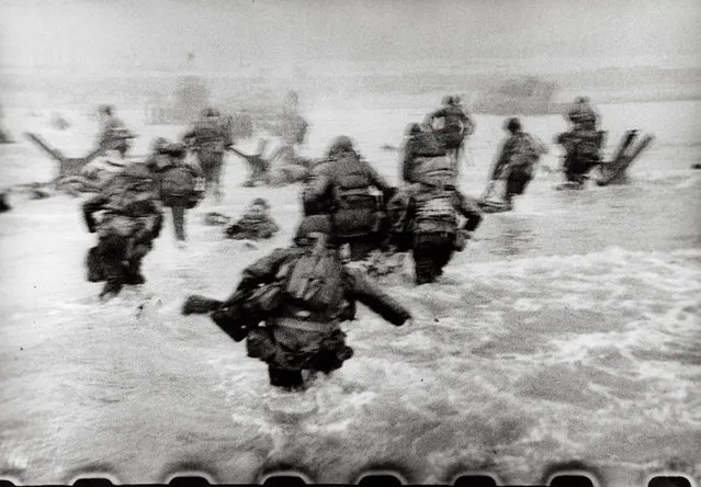 American soldiers landing on Omaha Beach, D-Day, Normandy, France, 6 June 1944, by Robert Capa. “The water was cold, and the beach still more than a hundred yards away. The bullets tore holes in the water around me, and I made for the nearest steel obstacle ... It was still very early and very grey for good pictures, but the grey water and the grey sky made the little men, dodging under the surrealistic designs of Hitler’s anti-invasion brain trust, very effective”. Robert Capa, Slightly Out of Focus (1947). (Photo by Robert Capa/International Center of Photography/Magnum Photos)