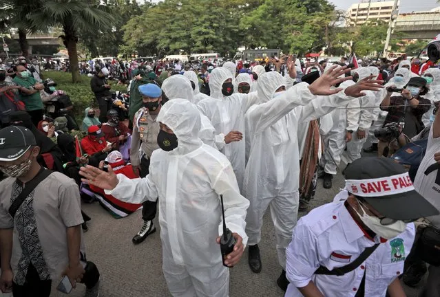 Police officers in protective suits gesture towards protesters to maintain their physical distance to help curb the spread of the coronavirus during an anti-Israel rally outside the U.S. Embassy in Jakarta, Indonesia, Tuesday, May 18, 2021. Pro-Palestinian protesters marched to the heavily guarded embassy on Tuesday to demand an end to Israeli airstrikes in the Gaza Strip. (Photo by Dita Alangkara/AP Photo)