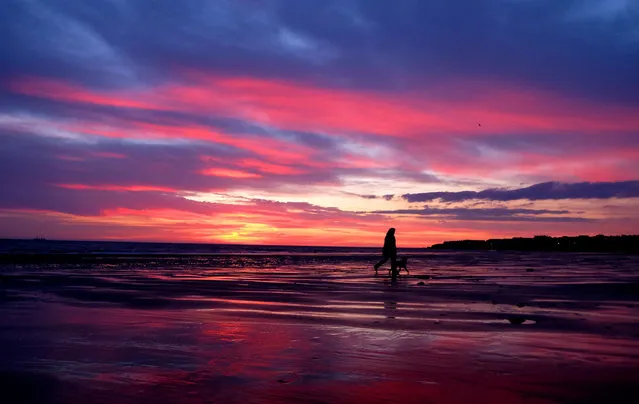 A woman walks her dog along the beach at sunrise in Whitley Bay, Tyne and Wear, UK on January 25, 2016. (Photo by Owen Humphreys/PA Wire)