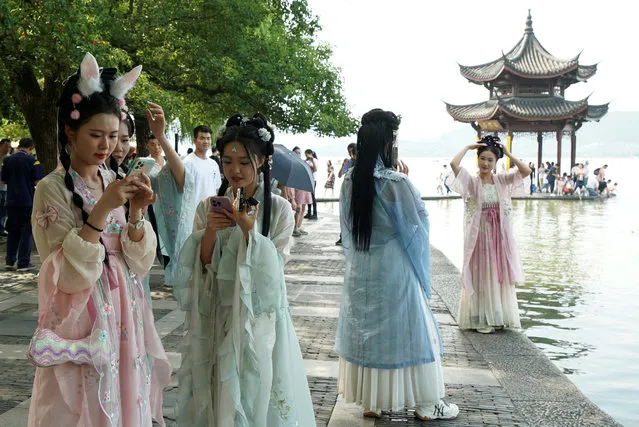 Women wearing traditional dresses look at their cellphones at West Lake during the first day of the holidays due to the Mid-Autumn Festival and National Day in Hangzhou, China on September 29, 2023. (Photo by Nicoco Chan/Reuters)