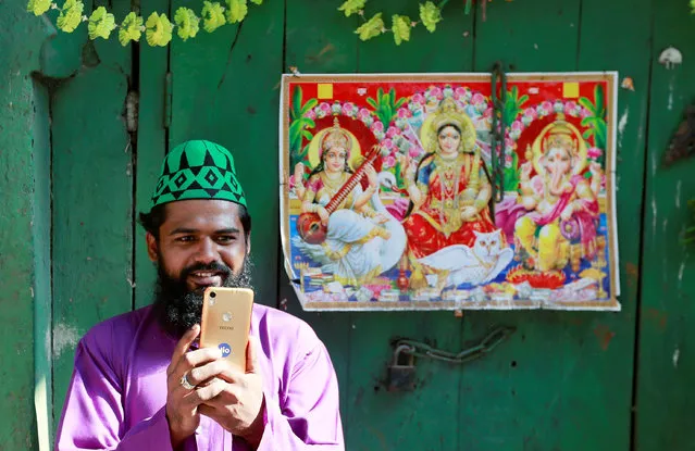 A Muslim man takes photographs with his mobile as he stands next to a picture of Hindu deities during a religious procession to mark Eid-e-Milad-ul-Nabi, or birthday celebrations of Prophet Mohammad, in the old quarters of Delhi, November 21, 2018. (Photo by Adnan Abidi/Reuters)