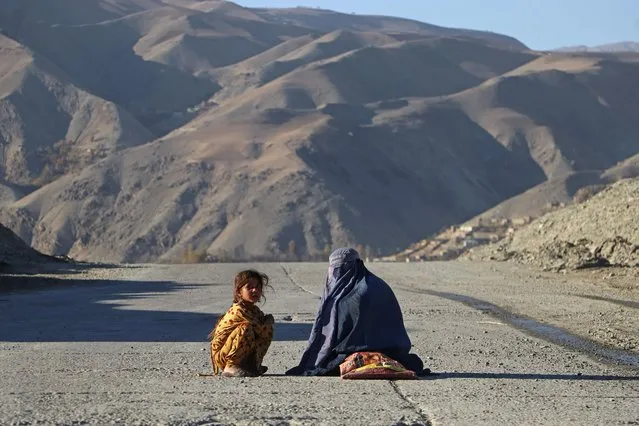 An Afghan burqa-clad woman sits beside a girl, as they look for alms along a street in the Fayzabad district of Badakhshan province on November 16, 2023. (Photo by Omer Abrar/AFP Photo)