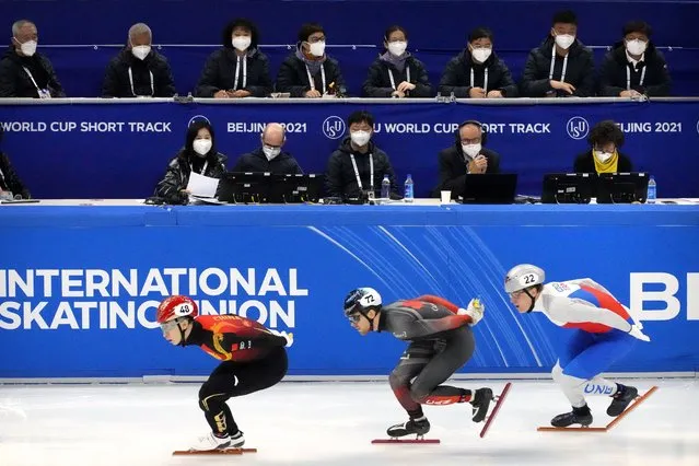 Race officials wearing face masks to protect against COVID-19 watch as skaters compete in a preliminary for men's 1000m at the ISU World Cup Short Track speed skating competition, a test event for the 2022 Winter Olympics, at the Capital Indoor Stadium in Beijing, Friday, October 22, 2021. (Photo by Mark Schiefelbein/AP Photo)
