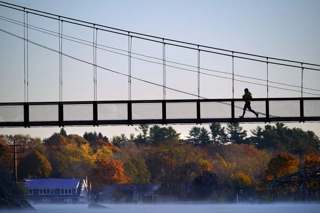 A jogger crosses the Swinging Bridge over the Androscoggin River on a frosty autumn morning, Thursday, November 4, 2021, in Brunswick, Maine. (Photo by Robert F. Bukaty/AP Photo)