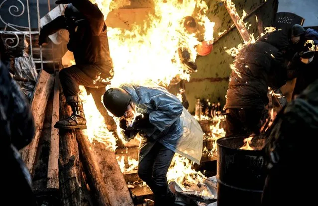 Protesters burn as they stand behind burning barricades during clashes with police on February 20, 2014 in Kiev. Ukraine's embattled leader announced a “truce” with the opposition as he prepared to get grilled by visiting EU diplomats over clashes that killed 26 and left the government facing diplomatic isolation. (Photo by Bulent Kilic/AFP Photo)
