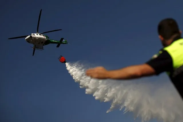 A helicopter drops water over a wildfire as a local police officer directs traffic on a road in Benahavis, southern Spain, May 19, 2015. (Photo by Jon Nazca/Reuters)