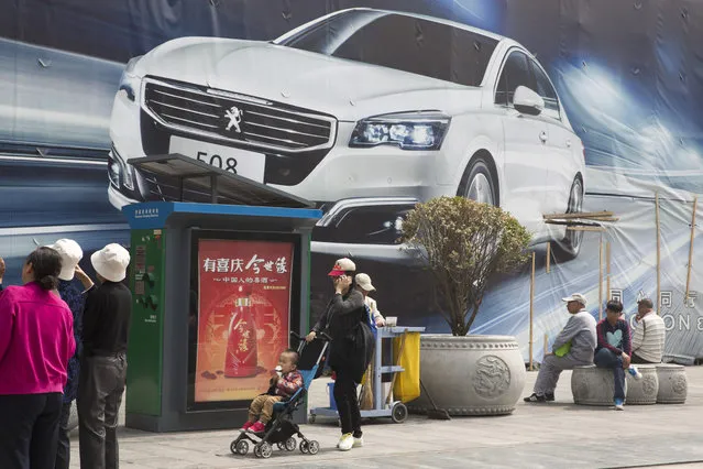 In this Wednesday, April 13, 2016 photo, a child eats ice cream as he is pushed past a car advertisement in Beijing. China's economic growth slowed in the first quarter to 6.7 percent compared with the previous year, according to official data released Friday, April 15, 2016. (Photo by Ng Han Guan/AP Photo)
