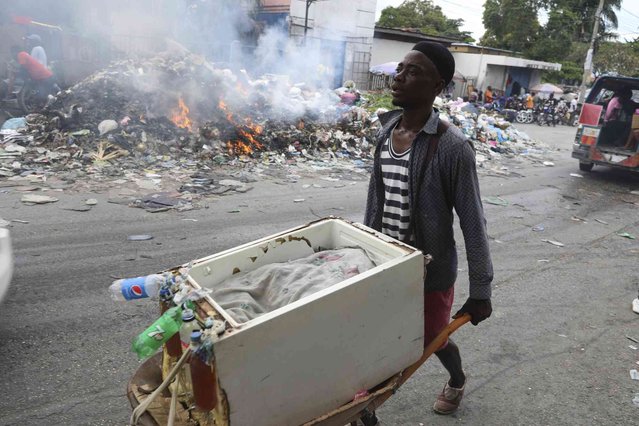 A street vendor uses a wheelbarrow to haul his container of beverages, past a pile of burning trash in Port-au-Prince, Haiti, Tuesday, April 30, 2024. (Photo by Odelyn Joseph/AP Photo)