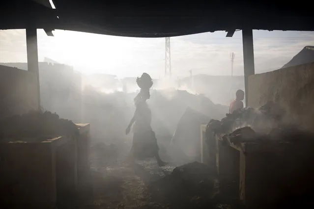 In this March 20, 2017 photo, a merchant walks in the smoke of a fire at a market in Port-au-Prince, Haiti. The fire raged at the biggest central market in the center of the Capital. (Photo by Dieu Nalio Chery/AP Photo)