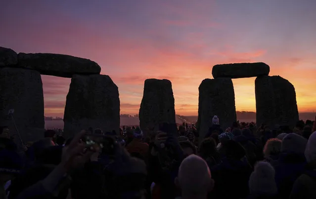The sun begins to rise behind the stones as people gather to take part in the winter solstice celebrations during sunrise at the Stonehenge prehistoric monument on Salisbury Plain in Wiltshire on Wednesday, December 22, 2021. (Photo by Andrew Matthews/PA Images via Getty Images)