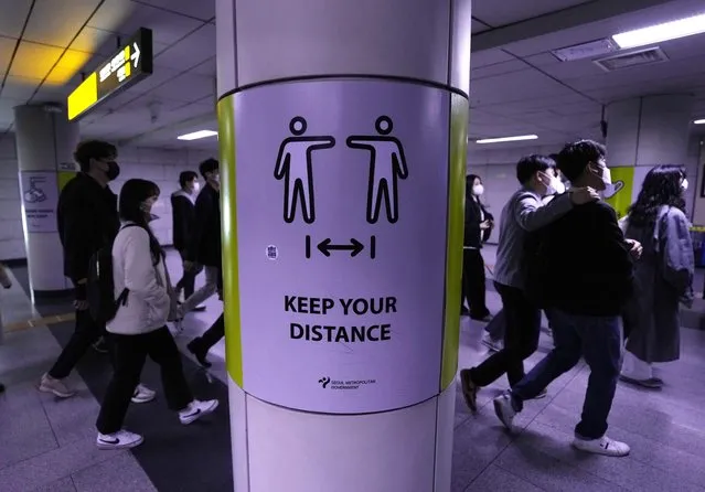 People wearing face masks pass by a poster reminding precautions against the coronavirus at a subway station in Seoul, South Korea, Friday, April 15, 2022. (Photo by Ahn Young-joon/AP Photo)