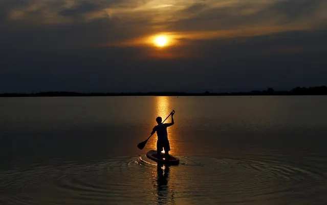 A boy is silhouetted as he paddles on a stand up board during sunset on Lake Zicksee in St. Andrae, Austria, July 24, 2015. (Photo by Leonhard Foeger/Reuters)