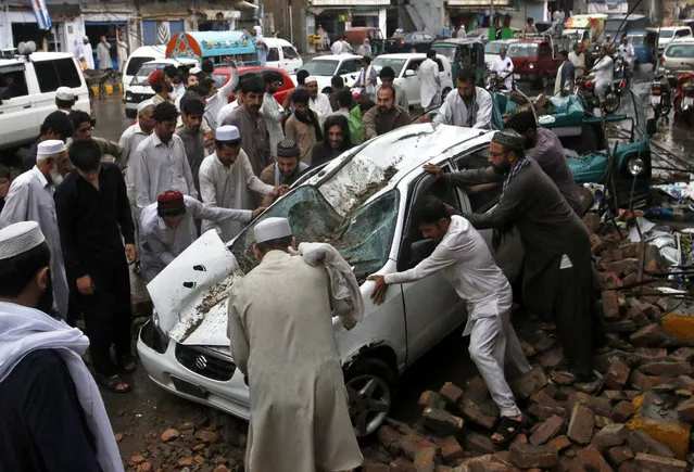 People push a car that was damaged by a collapsed wall in a heavy storm in Peshawar, Pakistan, Wednesday, June 15, 2016. Many people injured as heavy rain and wind damaged houses and felled trees, official said. (Photo by Mohammad Sajjad/AP Photo)