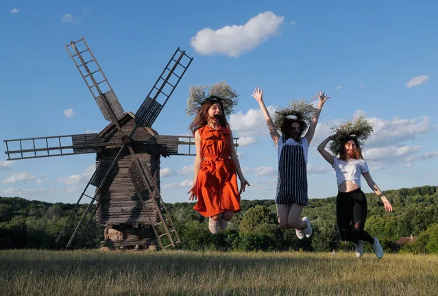 Ukrainian girls wearing flower's diadems jump in front of an old windmill in Kiev, Ukraine, 06 July 2019, as she celebrates the traditional pagan holiday of Ivana Kupala. Ivana Kupala is celebrated, during the summer solstice, on the shortest night of the year, marking the beginning of summer and is celebrated in Ukraine, Belarus, Poland and Russia. People sing and dance around bonfires, play games and perform traditional rituals. Young people jump over bonfires in order to test their bravery. Couples holding hands jump over the flames to test their love. If the couple does not succeed it is predicted to split up. Traditionally, children and young unmarried women wear wreaths of wild flowers on their heads to symbolize purity. (Photo by Sergey Dolzhenko/EPA/EFE)