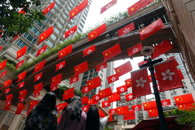 A woman takes pictures of Chinese and Hong Kong flags decorating a street, ahead of the 25th anniversary of the former British colony's handover to Chinese rule, in Hong Kong, China on June 30, 2022. (Photo by Joyce Zhou/Reuters)