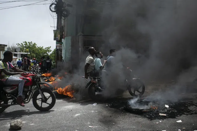 A motorcycle taxi driver carries clients past a burning barricade set by taxi drivers to protest the country's fuel shortage in Port-au-Prince, Haiti, Wednesday, July 13, 2022. (Photo by Odelyn Joseph/AP Photo)