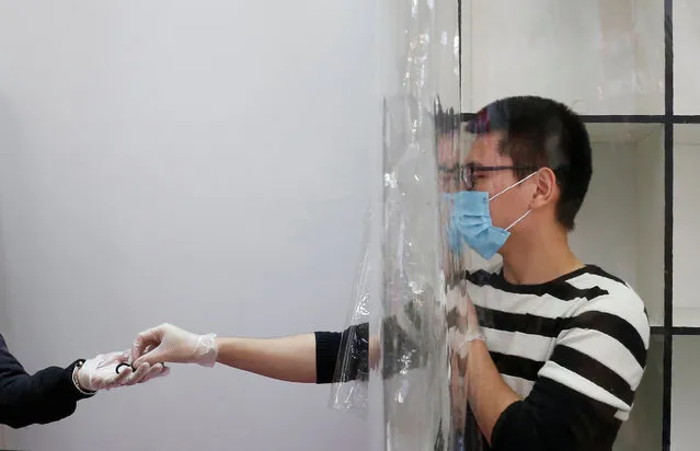 An employee of a store wears a face mask and work behind a plastic curtain as a precaution against the spread of the coronavirus disease (COVID-19) in Vina del Mar, Chile on March 14, 2020. (Photo by Rodrigo Garrido/Reuters)