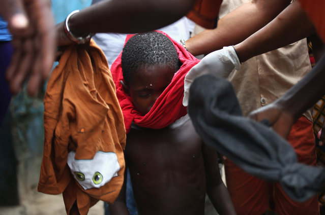 Local residents dress a sick Saah Exco, 10, after bathing him in a back alley of the West Point slum on August 19, 2014 in Monrovia, Liberia. According to communitey organizer John Saah Mbayoh, Saah's mother died of suspected but untested Ebola in West Point before he was brought to the isolation center the evening of August 13. (Photo by John Moore/Getty Images)