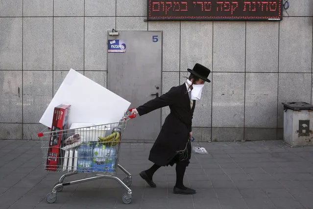 An ultra-Orthodox Jew wears an improvised protective face mask as he pulls a supermarket cart on a mainly deserted street because of the government's measures to help stop the spread of the coronavirus, in Bnei Brak, a suburb of Tel Aviv, Israel, Friday, April 3, 2020. The military plans to send troops in to assist local authorities with coronavirus control. (Photo by Oded Balilty/AP Photo)