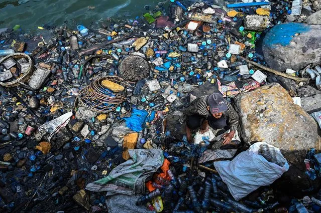 A man collects plastics in the water filled with garbages and oily wastes in Banda Aceh port on August 1, 2022. (Photo by Chaideer Mahyuddin/AFP Photo)