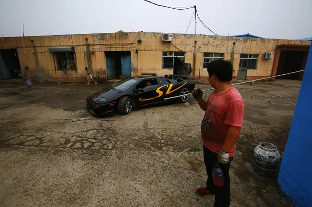 A man looks on as Wang Yu (C) drives a handmade replica of Lamborghini Diablo out of a garage on the outskirts of Beijing, August 21, 2014. (Photo by Petar Kujundzic/Reuters)