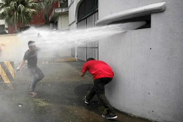 A youth activist throws paint bombs while being doused by firefighters at the gates of the Armed Forces of the Philippines (AFP) outside their headquarters in Camp Aguinaldo, Quezon City, metro Manila September 4, 2015. The group of activists threw paint bombs and vandalised the gates of the AFP's headquarters to protest against the supposed killing of indigenous people in Mindanao, southern Philippines, by members of the military, according to a press statement from the activists. (Photo by Al Falcon/Reuters)