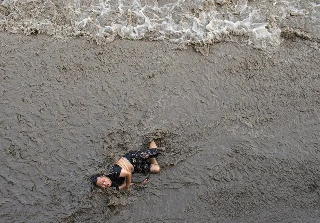 A man who fell off a bridge while waiting to watch tidal wave struggles as waves come towards him, on the banks of Qiantang River in Hangzhou, Zhejiang province, China, July 25, 2016. (Photo by Chance Chan/Reuters)