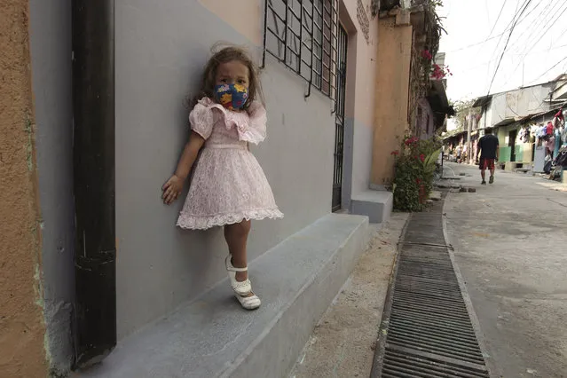 Five-year-old Fernanda Serrato poses in front of her house wearing a homemade mask to protect her from the spread of the new coronavirus, in the Papini community of San Salvador, El Salvador, Thursday, April 23, 2020. When the coronavirus appeared, President Nayib Bukele closed the borders and airports and imposed a mandatory home quarantine for all except those working in the government, hospitals, pharmacies or other designated businesses. People were allowed out only to buy groceries, and violators were detained, with more than 2,000 being held for 30-day stints. (Photo by Salvador Melendez/AP Photo)