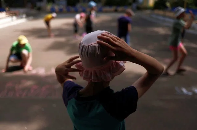 Tanya, 12, who is autistic and does not speak, watches other children draw with chalk in a play area at a facility for people with special needs, amid Russia's invasion of Ukraine, in Odesa, Ukraine, June 7, 2022. Tanya, like nine in 10 of the children in Ukraine's orphanage system, is a “social orphan” – children whose parents are unable to care for them or denied parental rights under Ukrainian law. (Photo by Edgar Su/Reuters)
