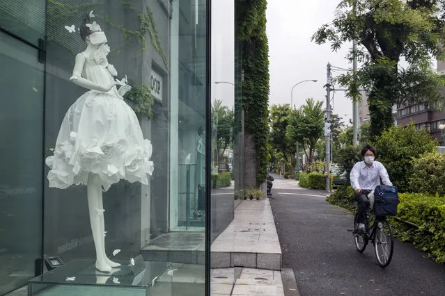 A man wearing a protective mask to help curb the spread of the coronavirus passes by a window display of a dress on a mannequin with a similar mask, Friday, July 17, 2020, in Tokyo. The Japanese capital has confirmed Friday more than 290 new coronavirus cases. (Photo by Kiichiro Sato/AP Photo)