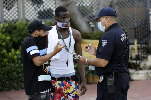 A man covers his nose with his shirt, left, as Luis Negron, a Miami Beach code compliance officer, right, talks to him about wearing a protective face mask amid the coronavirus pandemic, Friday, July 24, 2020, on Ocean Drive in Miami Beach, Fla. Masks are mandated both indoors and outdoors in Miami Beach. People found not wearing a mask are subject to a civil fine of $50. (Photo by Lynne Sladky/AP Photo)