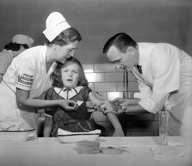 Seven-year-old Mimi Meade winces from the sting as Dr. Richard Mulvaney inoculates her April 26, 1954 in McClean, Va., with the new Salk polio vaccine.  Mrs. John Lucas, a registered nurse, holds Mimi's arm steady as she gets one of the first injections of the countrywide test. (Photo by Harvey Georges/AP Photo)