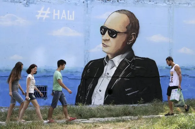 People walk past a graffiti depicting Russian President Vladimir Putin seen on a residential building in Simferopol, Crimea, August 19, 2015. The sign on the graffiti reads “Ours”. (Photo by Pavel Rebrov/Reuters)