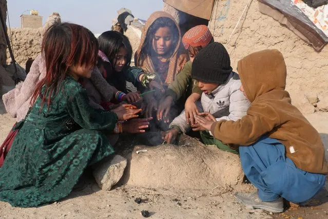 Afghan internally-displaced children warm-up around a fire outside their temporary mud house on the outskirts of Herat province on December 6, 2022. (Photo by Mohsen Karimi/AFP Photo)