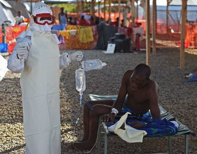 A nurse wearing personal protective equipment (PPE) assists an ebola patient at the Kenama treatment center run by the Red Cross Society on November 15, 2014. Ebola-hit Sierra Leone faces social and economic disaster as gains made since the country's ruinous civil war are wiped out by the epidemic, according to a major study released on November 13. (Photo by Francisco Leong/AFP Photo)
