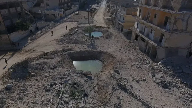 A still image taken on September 27, 2016 from a drone footage obtained by Reuters shows people standing near craters and damaged buildings in a rebel-held area of Aleppo, Syria. (Photo by Reuters TV)