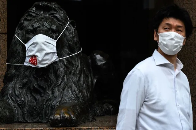 A man wearing a face mask walks past a faced mask-clad lion statue of a department store in Ginza district of Tokyo on September 29, 2020. (Photo by Philip Fong/AFP Photo)