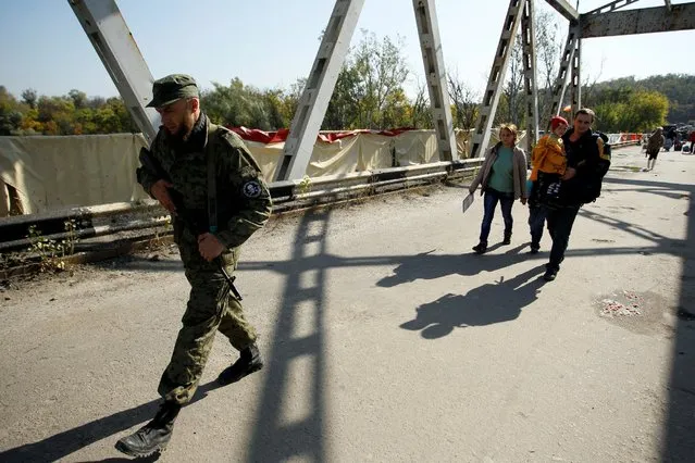 People are escorted by a member of the self-proclaimed Luhansk People's Republic forces as they walk along a bridge located on the troops contact line between pro-Moscow rebels and Ukrainian troops, in the settlement of Stanytsia Luhanska in Luhansk region, Ukraine, October 1, 2016. (Photo by Alexander Ermochenko/Reuters)