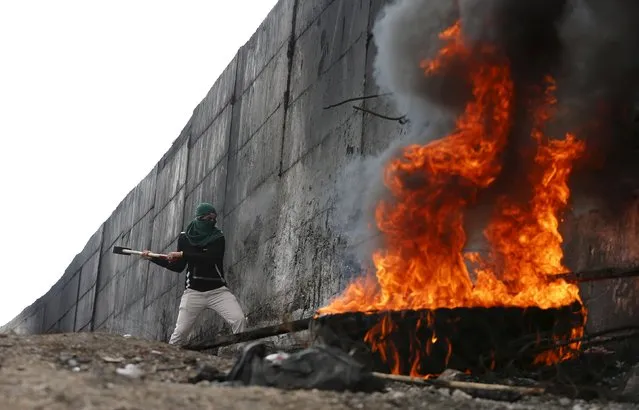 A Palestinian protester tries to hammer a hole through the Israeli barrier that separates the West Bank town of Abu Dis from Jerusalem, during clashes with Israeli troops October 28, 2015. (Photo by Ammar Awad/Reuters)