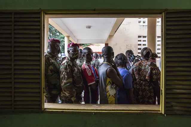 Civilians and soldiers line up to vote at a school in Conakry, Guinea, Sunday October 18, 2020. Guineans head to the polls to elect their president, choosing between incumbent Alpha Conde who is seeking a third term and historical opponent Cellou Dalein Diallo. (Photo by Sadak Souici/AP Photo)