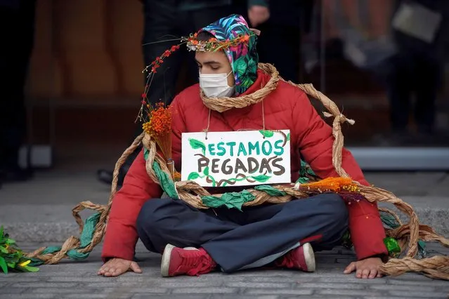 An activist of environmental protest group Extinction Rebellion (XR) sits at the entrance of the Agriculture Ministry headquarters after sticking their hands to the pavement and showing a sign thet reads “We are glued” during a protest demanding the Spanish government to protect biodiversity in Madrid on November 4, 2020. (Photo by Oscar del Pozo/AFP Photo)