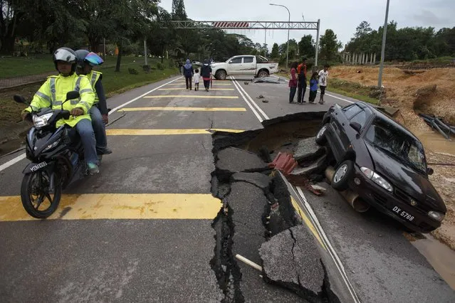 People ride past a road damaged by flooding at Kuala Krai in Kelantan December 30, 2014. The worst flooding in Malaysia in more than a decade has killed 10 people and forced nearly 160,000 from their homes and more rain is expected, authorities said on Sunday. (Photo by Athit Perawongmetha/Reuters)