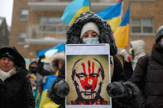 A woman holds a portrait of Russian president Vladimir Putin with a bloody hand on his face as members of the Ukrainian community protest in front of the Consulate General of the Russian Federation on February 25, 2022 in Montreal, Quebec. The community gathered to protest the ongoing attacks by Russian soldiers in Ukraine. (Photo by Andrej Ivanov/AFP Photo)