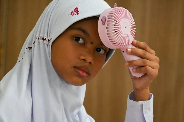 A primary school student uses a portable fan to keep cool in a classroom during hot weather in Banda Aceh on May 15, 2023. (Photo by Chaideer Mahyuddin/AFP Photo)
